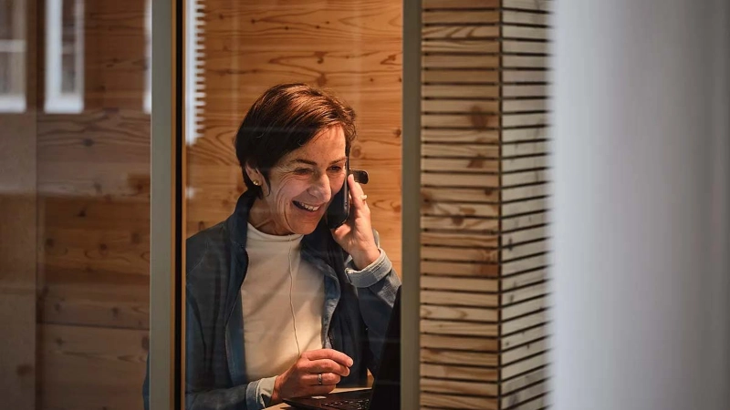 Eine lächelnde ältere Frau sitzt im Büro und telefoniert Eine lächelnde ältere Frau sitzt im Büro und telefoniert