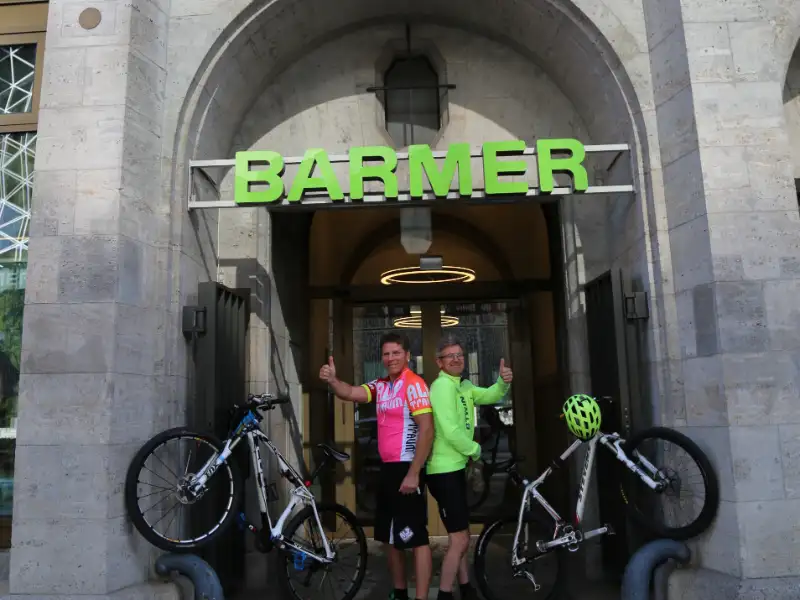 Zwei Barmer Mitarbeiter, die mit ihren Fahrräder ein V in der Eingangspforte von Barmer bilden Zwei Barmer Mitarbeiter, die mit ihren Fahrräder ein V in der Eingangspforte von Barmer bilden