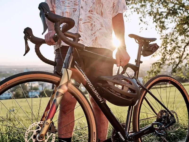 Close Up auf einen Mann, der ein neues Gravelbike hält, er steht auf einer Sonnendurchfluteten Wiese Close Up auf einen Mann, der ein neues Gravelbike hält, er steht auf einer Sonnendurchfluteten Wiese